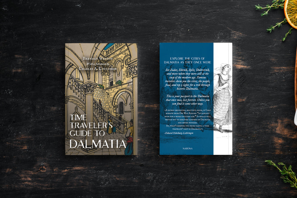 A book titled 'The Time Traveler's Guide to Dalmatia' shown alongside a matching travel card or insert on a dark wooden surface. The book cover features an illustration of a historic interior with arches and stairs, while the insert has a blue vertical band with white text and a black-and-white illustration of a woman.