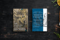 A book titled 'The Time Traveler's Guide to Dalmatia' shown alongside a matching travel card or insert on a dark wooden surface. The book cover features an illustration of a historic interior with arches and stairs, while the insert has a blue vertical band with white text and a black-and-white illustration of a woman.